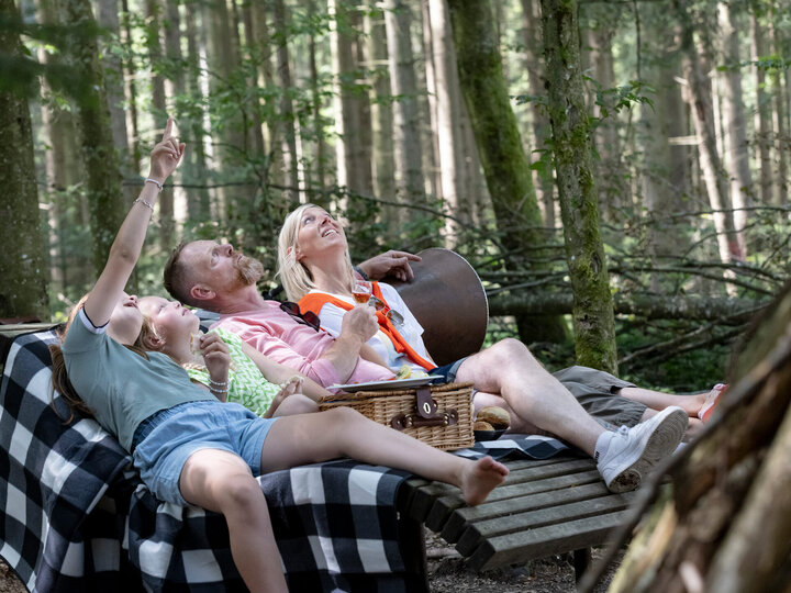 Eine Familie entspannt auf einer Liege im Wald.