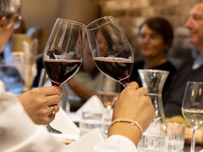 Zwei Personen halten je ein Glas Rotwein in der Hand.
