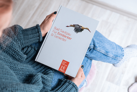 Eine Frau hält ein Buch mit dem Titel "Bad Saulgau: Für Entdecker & Genießer".